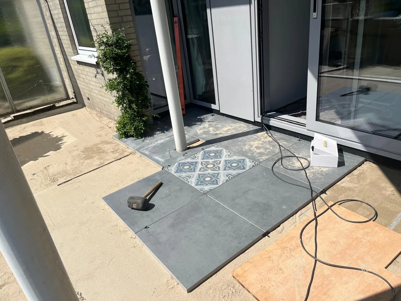 New patio being laid outside a garden room, with plain grey tiles and one patterned decorative tile as an accent