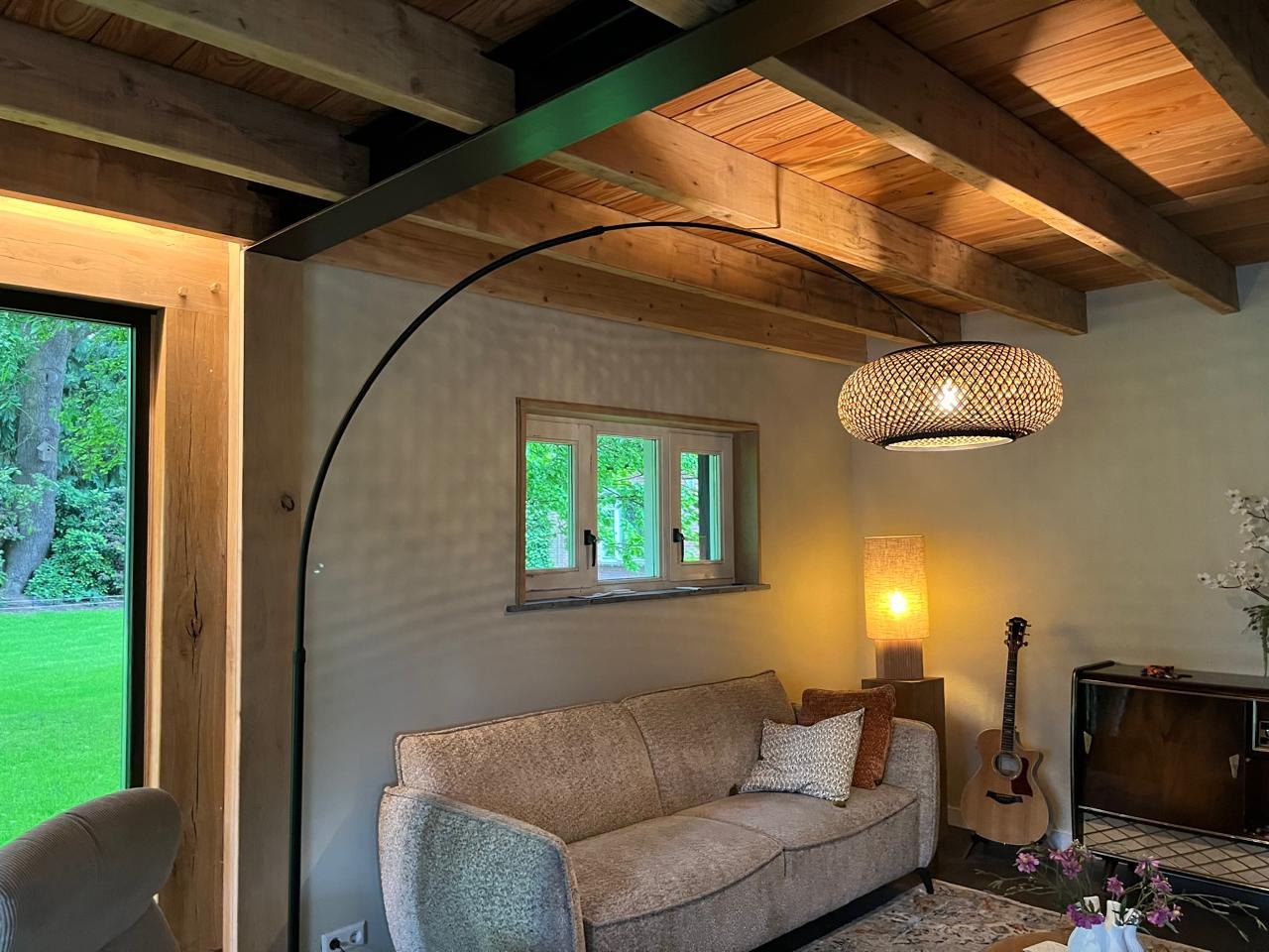 Finished living room with an exposed timber beam ceiling, an arched floor lamp and a view onto the garden